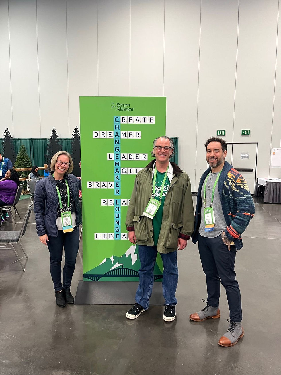 Three conference attendees posing beside a Scrum Alliance banner
